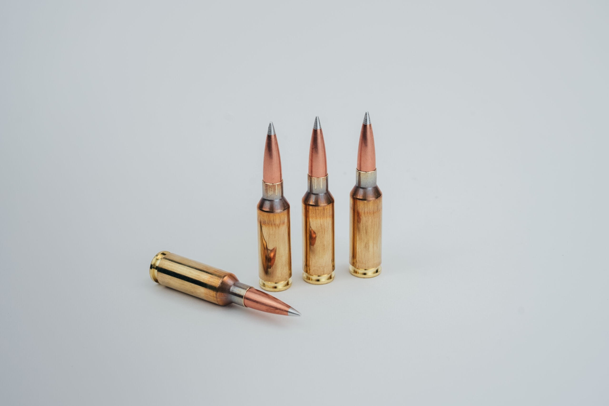 image0 - Make Ready Munitions Three copper rifle bullets standing upright with a fourth lying on its side on a light gray background.