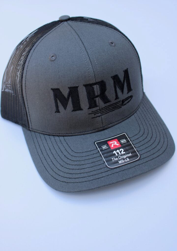 Dark gray trucker cap with black embroidered 'MRM' logo on the front panel, mesh back, and sticker on the curved brim scene.